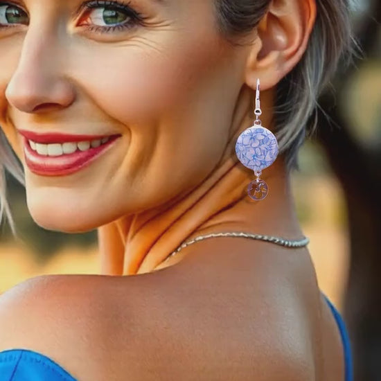 en video une jeune femme portant les boucles d'oreilles en email sur cuivre aux motifs  floraux légers hibiscus  bleus prolongé par une breloque en argent hibiscus. Bijou artisanal émaillé à la main chez maison CALUB les émaux du Luberon