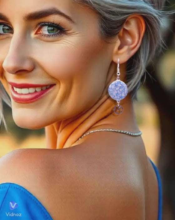 en video une jeune femme portant les boucles d'oreilles en email sur cuivre aux motifs  floraux légers hibiscus  bleus prolongé par une breloque en argent hibiscus. Bijou artisanal émaillé à la main chez maison CALUB les émaux du Luberon