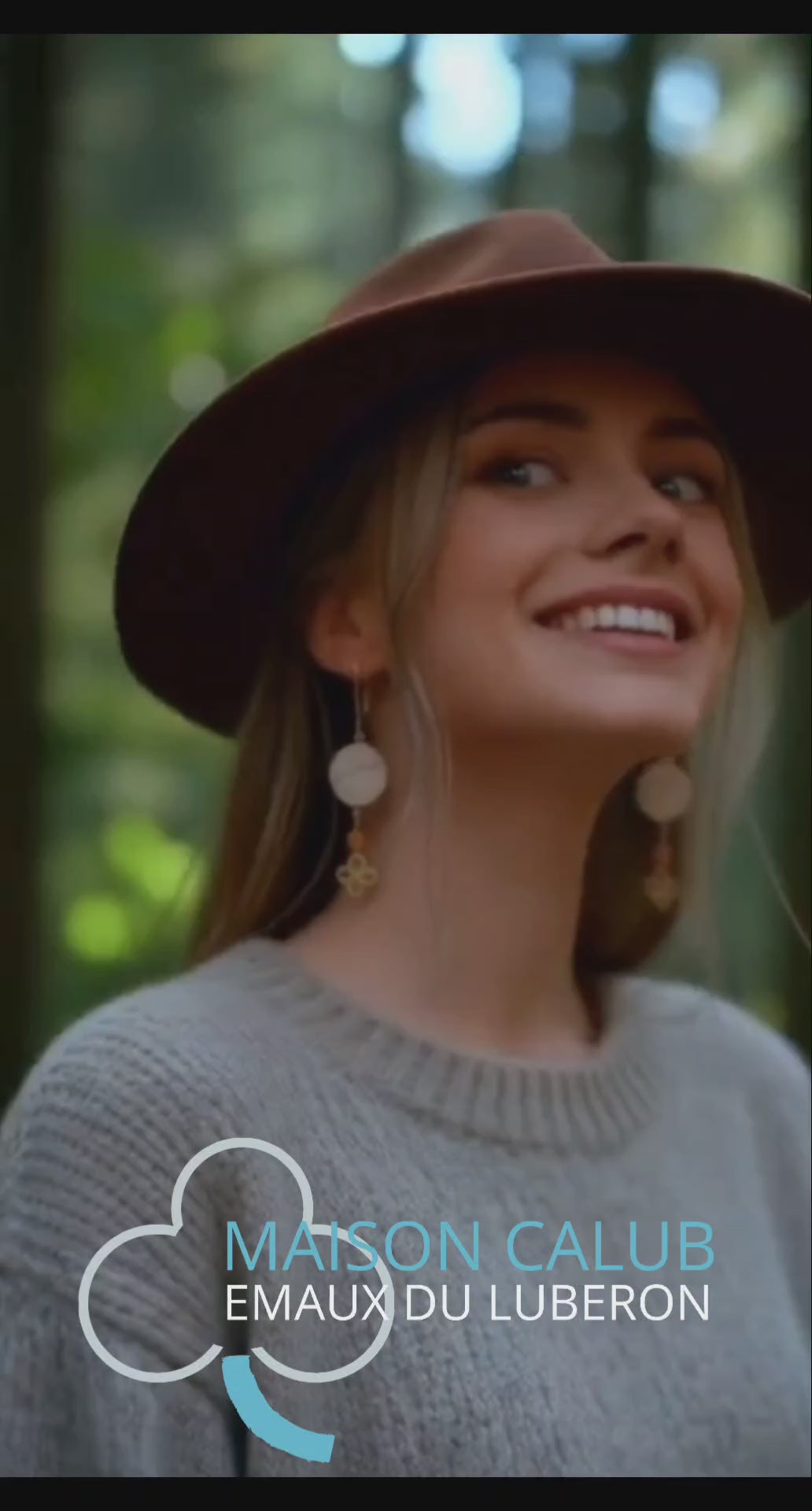 vidéo d'une jeune femme portant les boucles d'oreilles en émail sur cuivre - bijou artisanal français évoquant la silhouette de la montagne sainte victoire à Aix-en-Provence, d'une simple ligne noire sur fond blanc.Breloque dorée et perle en verre