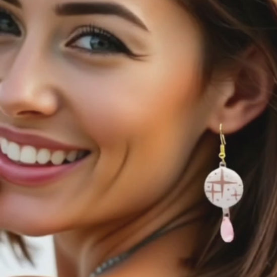video d'une jeune femme portant les boucles d'oreilles en émail sur cuivre aux motif d'étoiles rosés sur blanc prolongé par une perle de verre goutte. Bijou artisanal fait à la main chez maison calub les emaux du Luberon