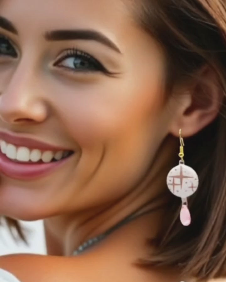 video d'une jeune femme portant les boucles d'oreilles en émail sur cuivre aux motif d'étoiles rosés sur blanc prolongé par une perle de verre goutte. Bijou artisanal fait à la main chez maison calub les emaux du Luberon